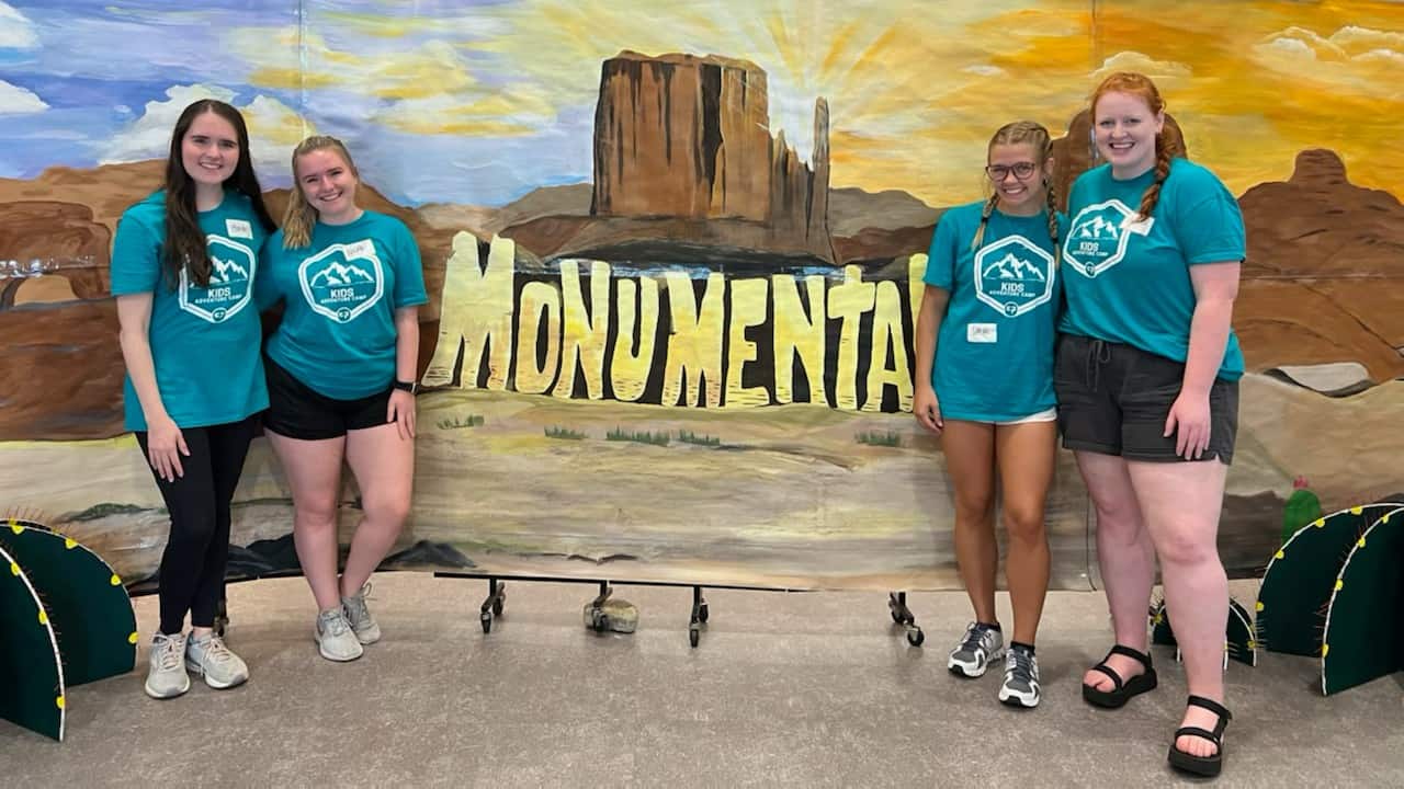 AccelerateInternship_07 Interns in front of VBS backdrop that says Monumental